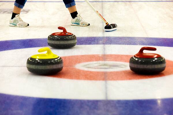 Curling stones on an ice rink with a player sweeping in the background.