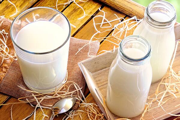 Glass and bottles of fresh milk on a wooden table.