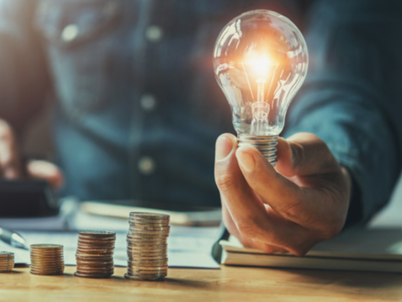 Business man holding light bulb on the desk in office and calculating on calculator